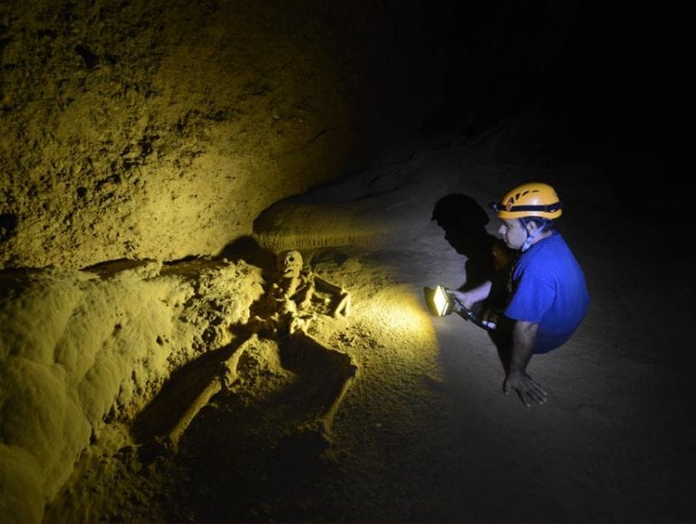 Pacz Tours guide using a headlamp to illuminate the Crystal Maiden skeleton in the ATM Cave, Belize