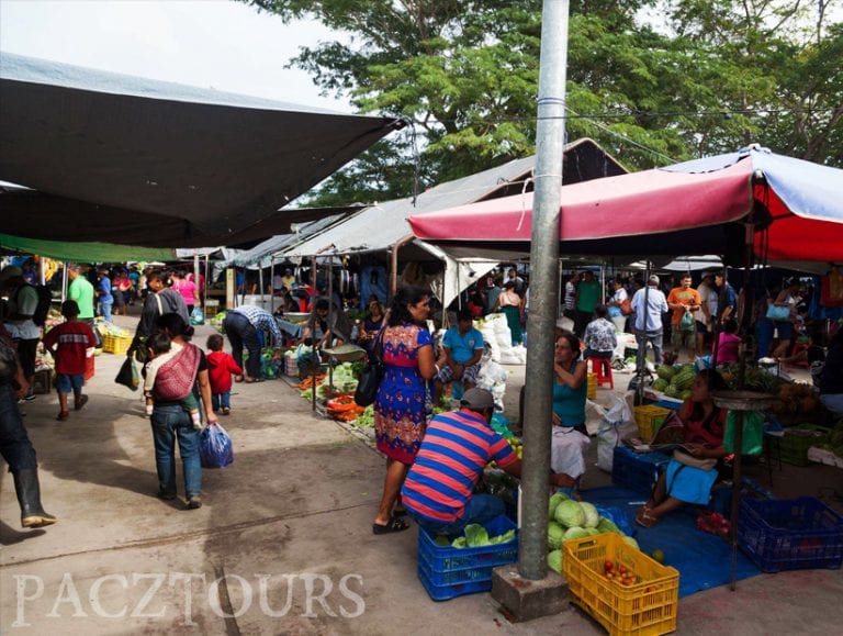 Colorful market scene in San Ignacio, Belize with vendors selling fresh produce under umbrellas and tarps for shade
